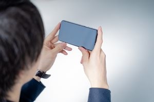 スマホで動画視聴する20代男性-リビングのソファーに座りリラックス