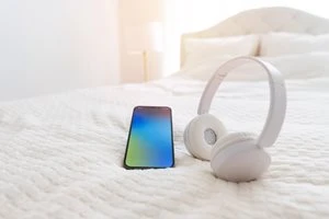 明る部屋の白いベッドにスマホとヘッドフォン